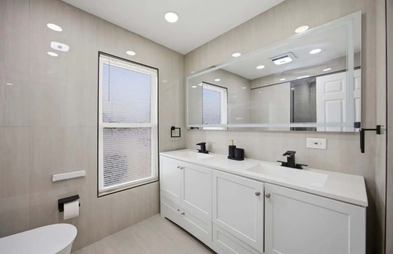 A finished bathroom with a floating double vanity, a full width mirror and large format stone running to the ceiling