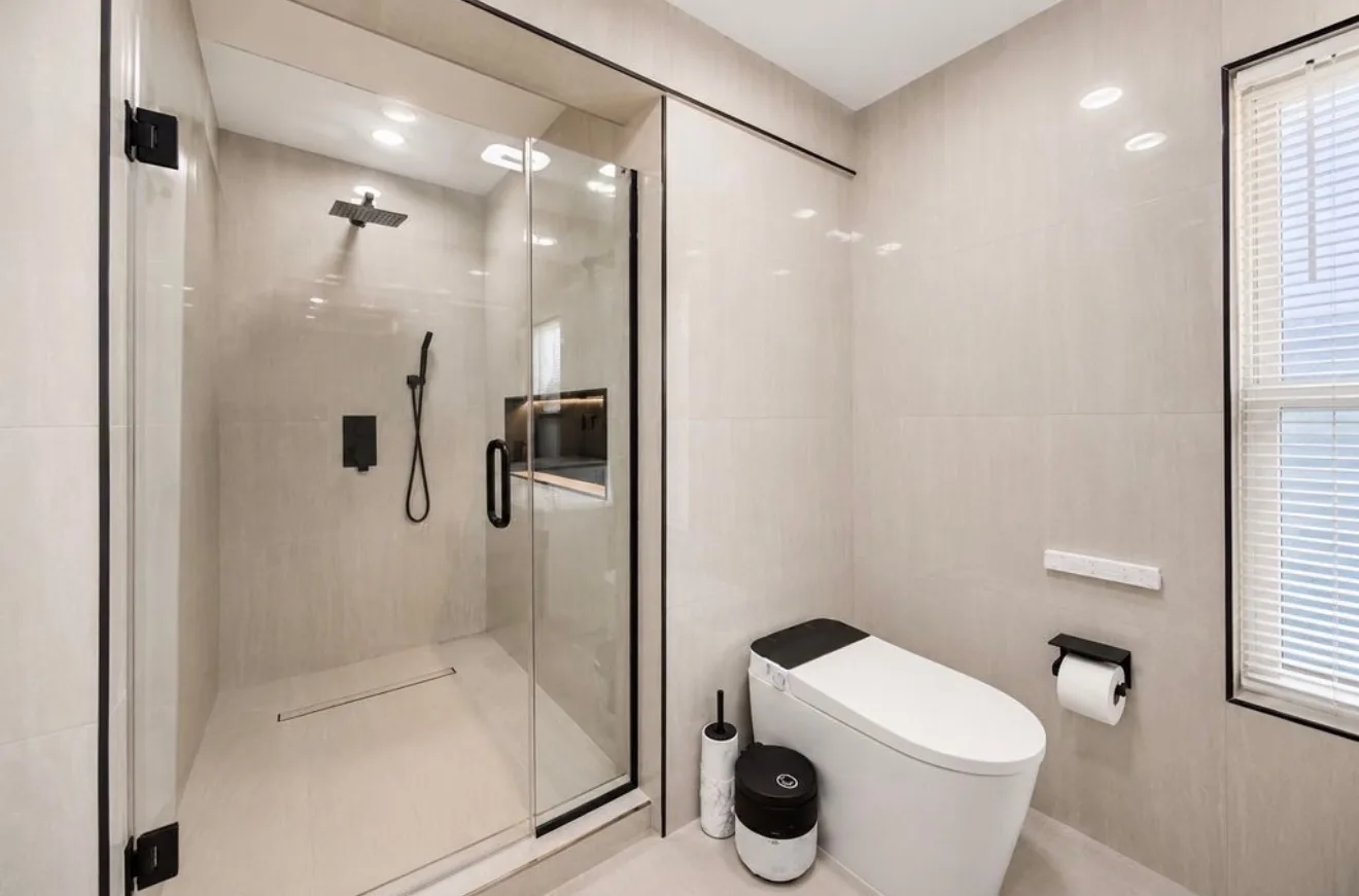 The walk in shower in the same bathroom, with a black rain head, a linear drain and a low tiled curb
