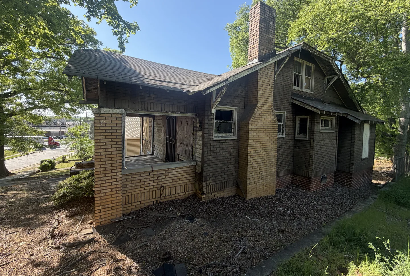 A derelict gambrel roofed house in Birmingham before renovation, its walls covered in peeling brick patterned asphalt siding and its windows boarded over
