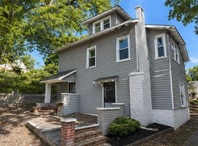 The second house after renovation, in grey lap siding with the brick corner pier painted white and new entry steps rebuilt
