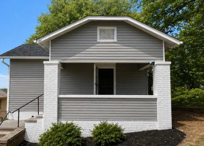 The street front after renovation, with new siding, white painted brick porch piers, a new storm door and planting beds