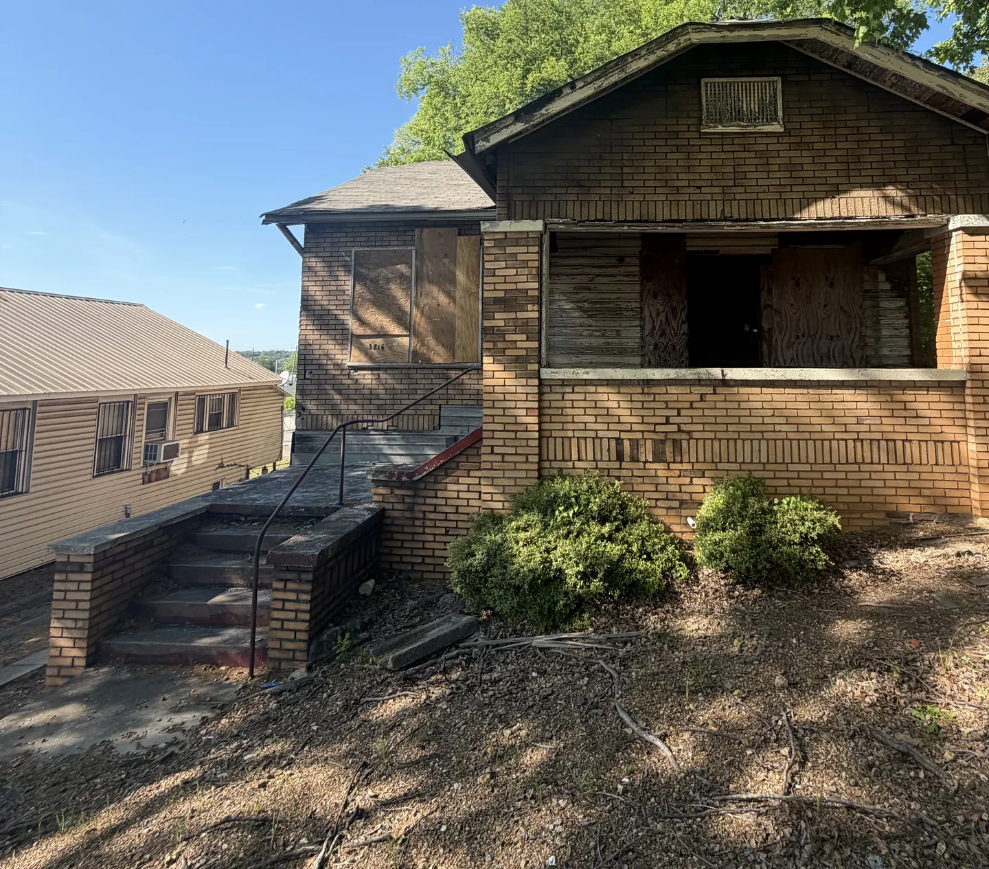 The street front of the same house before work, with plywood over the porch openings and a bare dirt yard