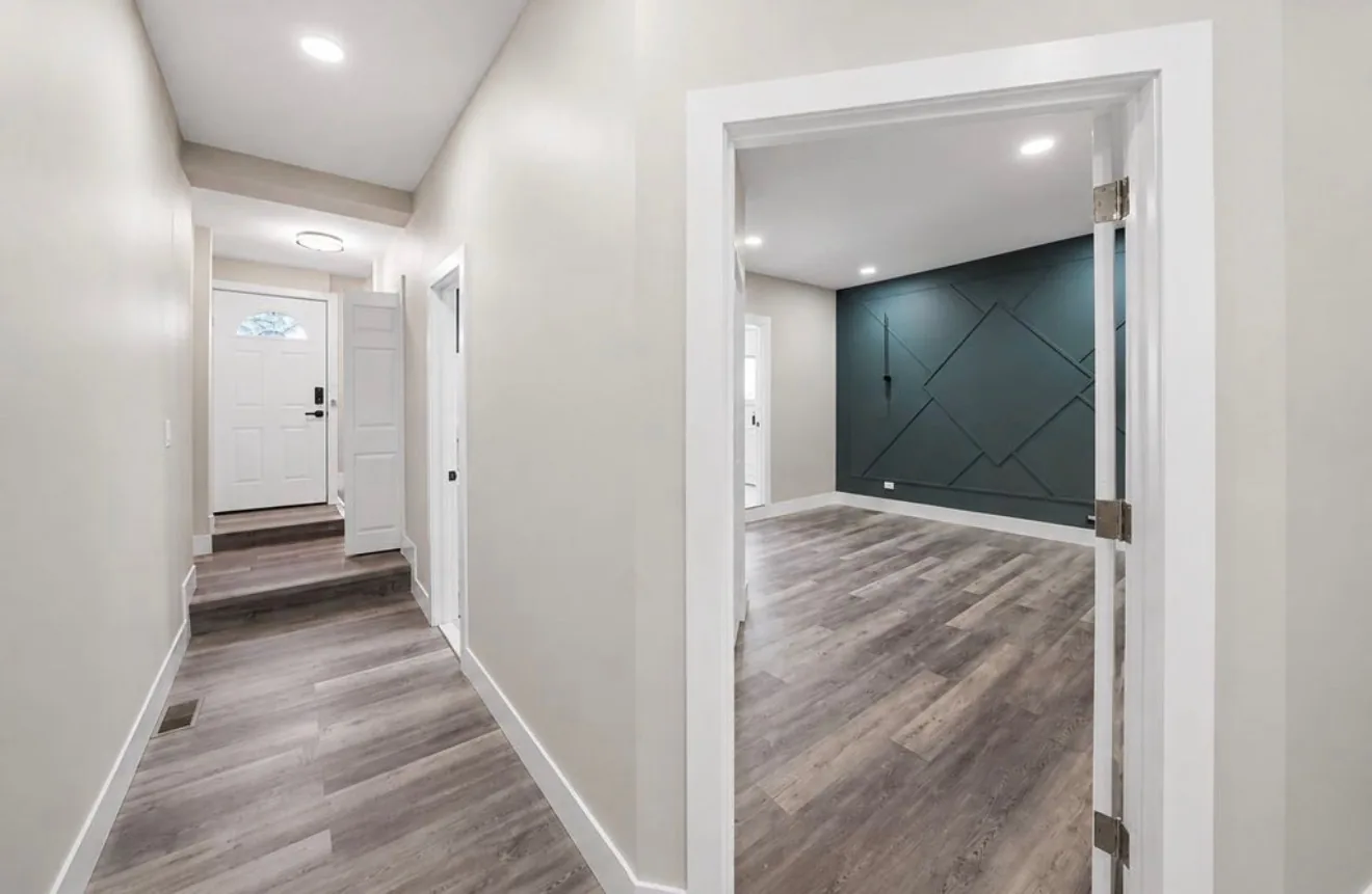 A hallway looking towards a front door with a fanlight, opening into a teal panelled room