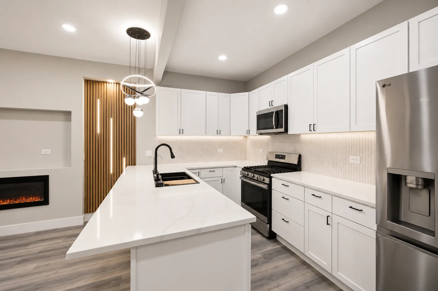 A finished kitchen with white shaker cabinets, a fluted stone backsplash lit from beneath the upper cabinets, and a black island sink
