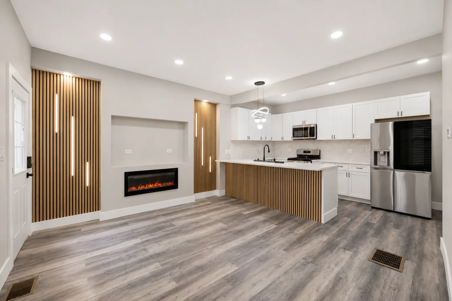 An open plan kitchen and living space with slatted timber feature walls, inset vertical light strips and a linear fireplace set into a plaster niche