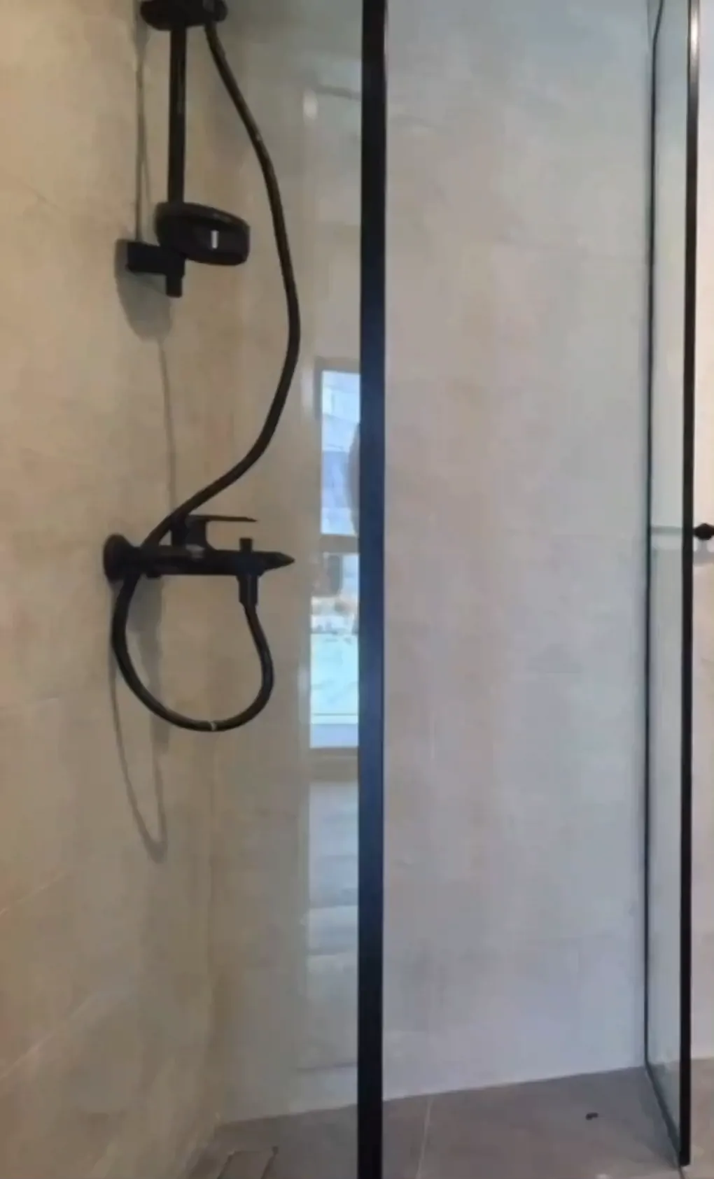 A finished bathroom filmed in one pass: a curved glass shower enclosure, large format stone run wall to wall, a wall hung pan and a floating vanity