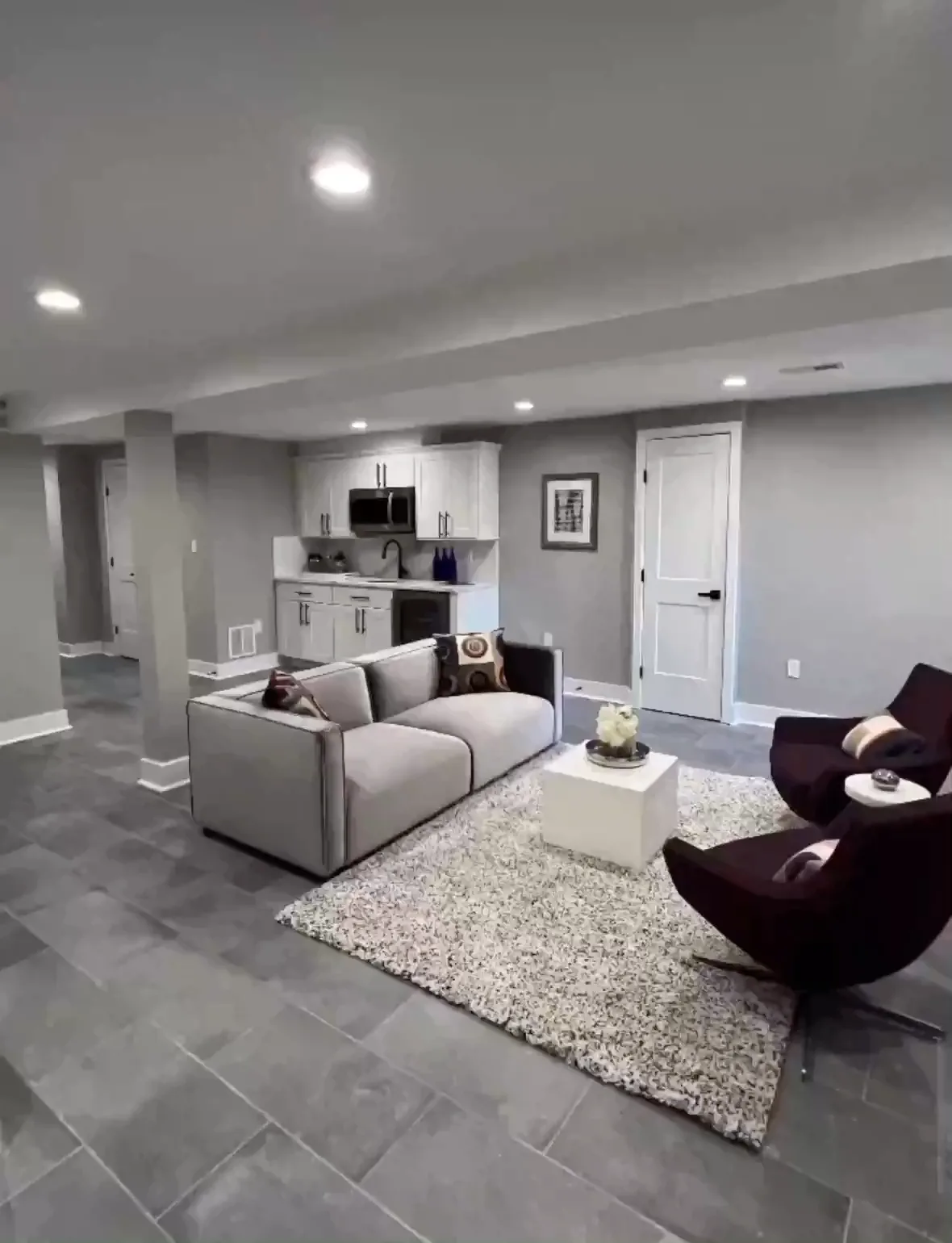 A finished open living space with a wet bar, shaker cabinets, a stone counter and large format tile flooring