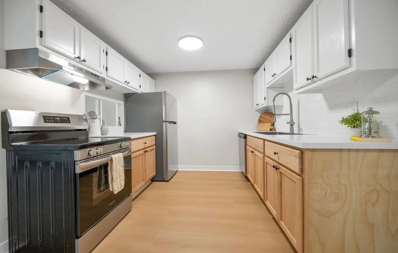 A renovated apartment kitchen at Remington with white upper cabinets, natural birch lowers and a subway tile backsplash