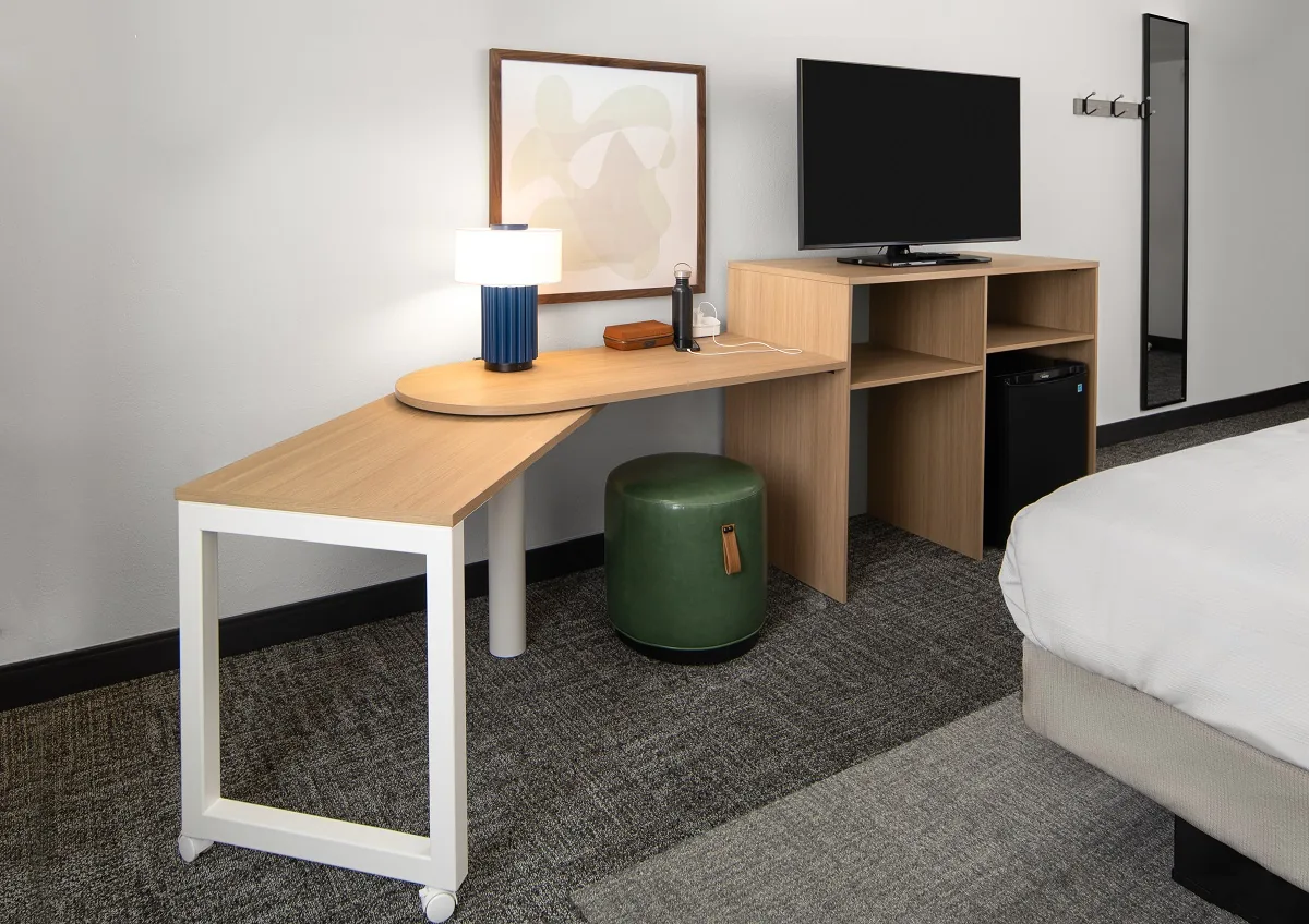 The work zone in a Spark by Hilton guest room, an oval topped desk that swings out from an open oak credenza