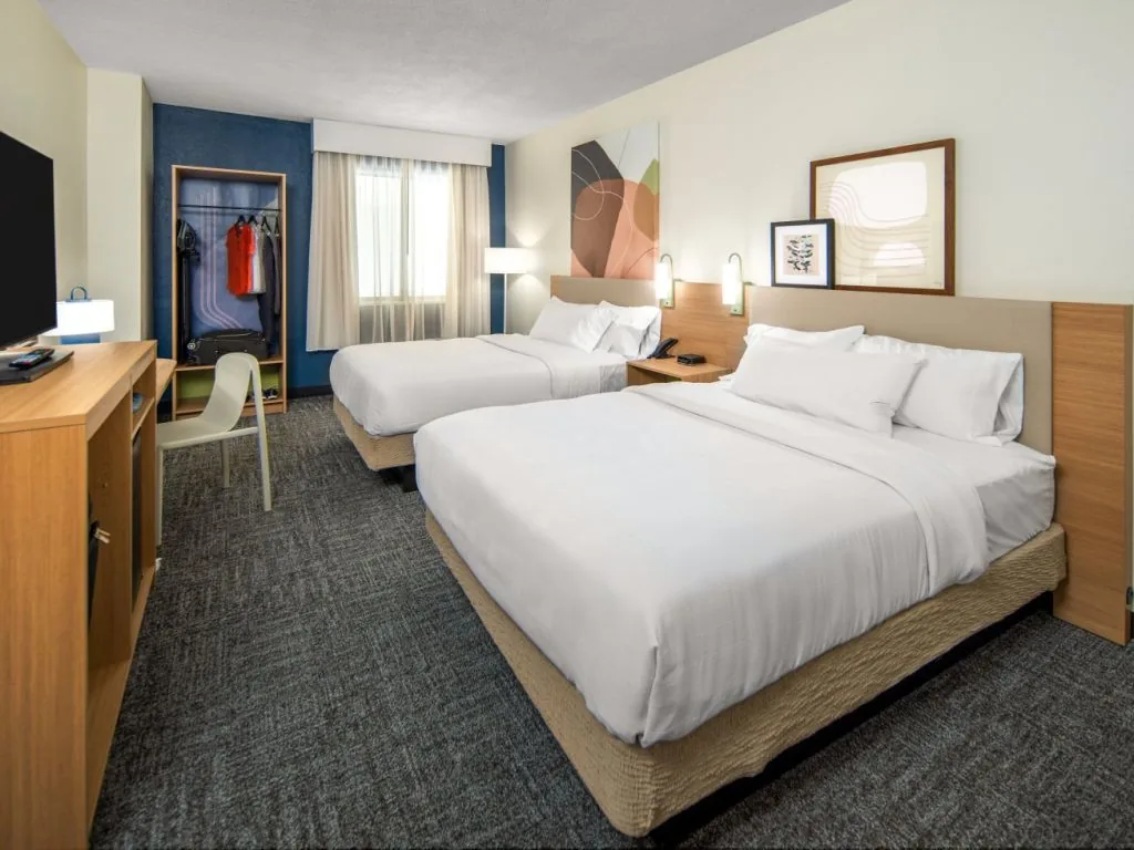 A finished double queen guest room at Spark by Hilton with an open oak wardrobe and wall mounted reading lights
