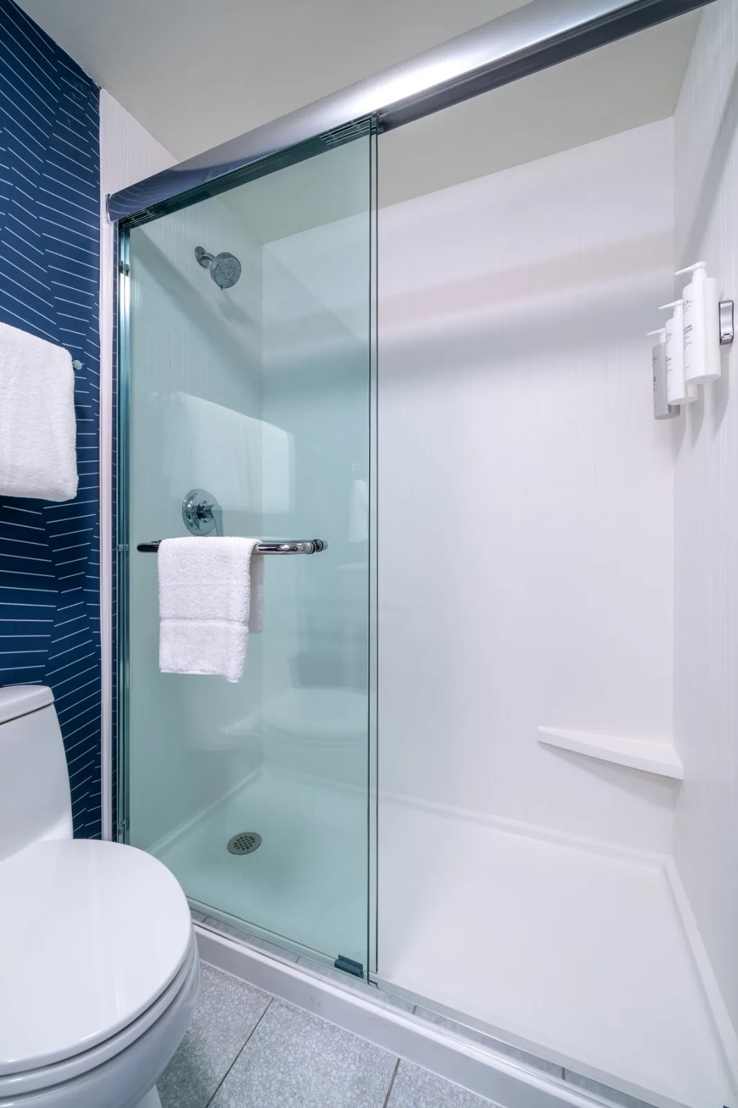 A guest bathroom shower at Spark by Hilton with a white surround and framed sliding glass doors