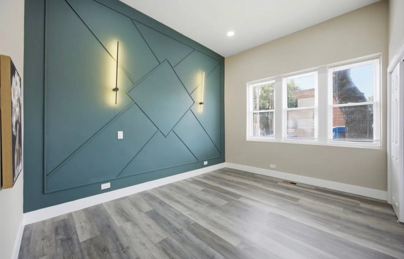 A finished bedroom with a deep teal feature wall built from applied panel moulding, two slim vertical wall lights and a bank of three windows