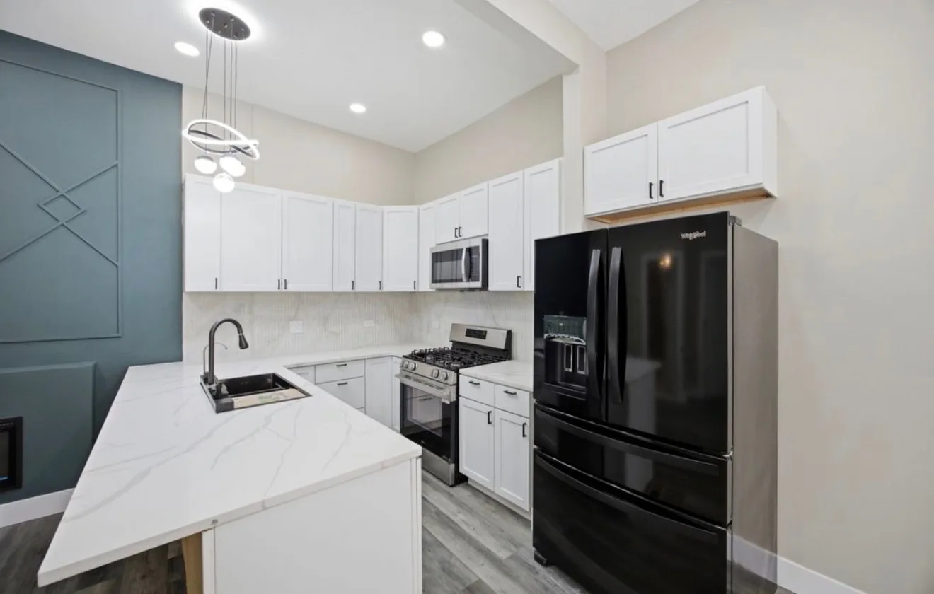 The kitchen in the same home, with a veined quartz waterfall counter, a black undermount sink and stacked stone tile behind the range