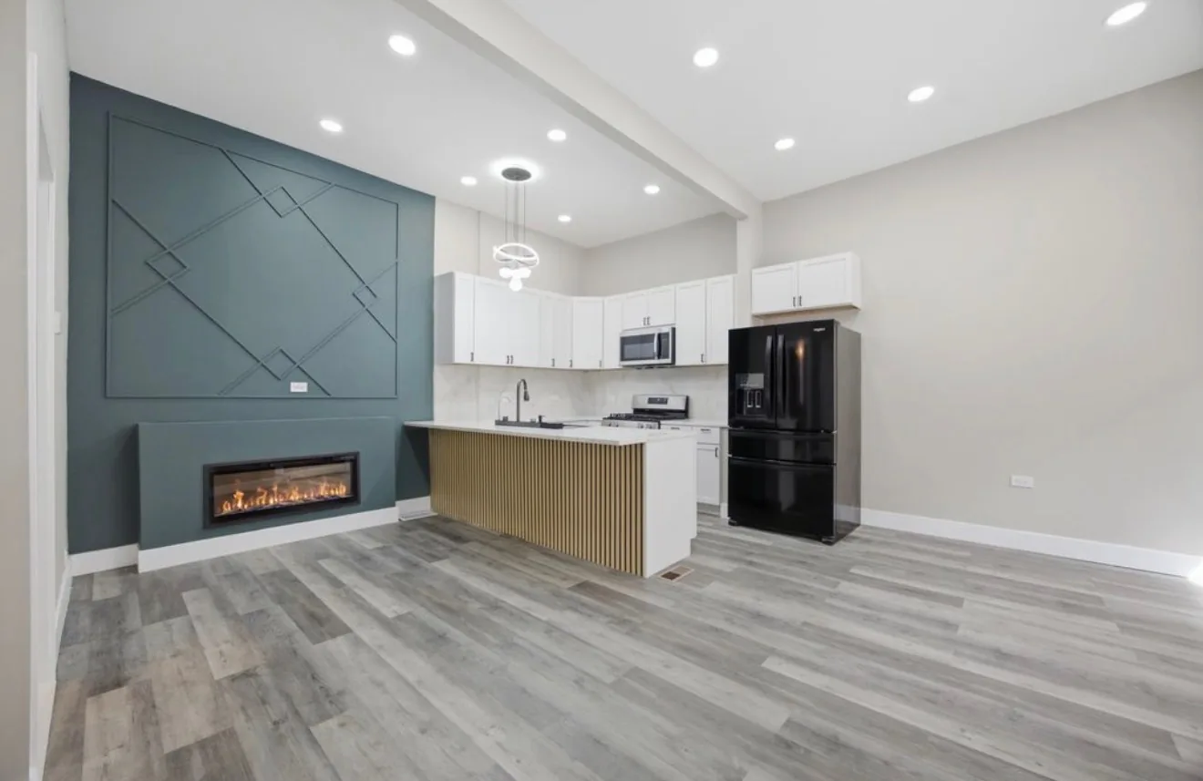 A living space with a teal panelled feature wall, a linear fireplace and a kitchen island finished with a fluted timber end panel
