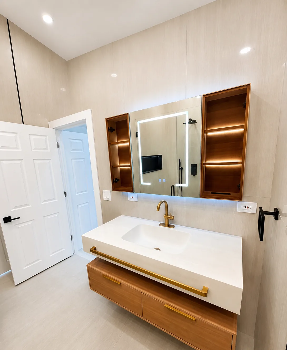 The vanity wall of the same bathroom with the mirrored cabinets open, showing lit glass shelves